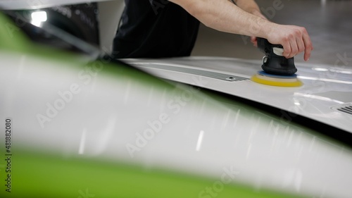 Worker with orbital polisher in auto repair shop closeup. Professional car polishing.