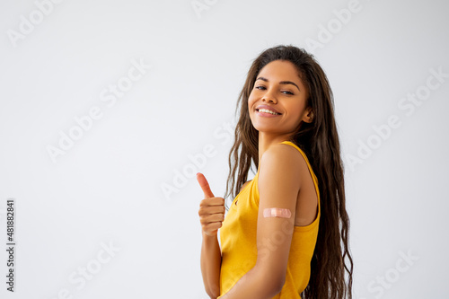 Happy Young Woman standing against light background showing her arm with Bandage. Black woman received a Vaccine. Studio shot   photo