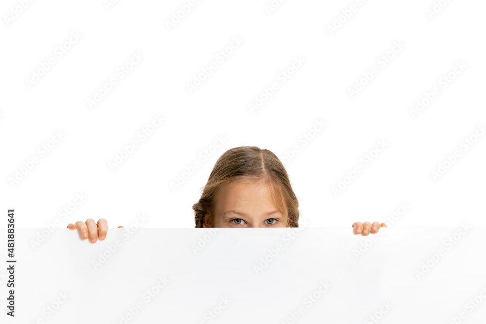 Funny child, little girl, pupil in casual style clothes peeking out from behind wall isolated on white background. Concept of childhood, emotions, study Funny child, little girl, pupil in casual style clothes peeking out from behind wall isolated on white background. Concept of childhood, emotions, study