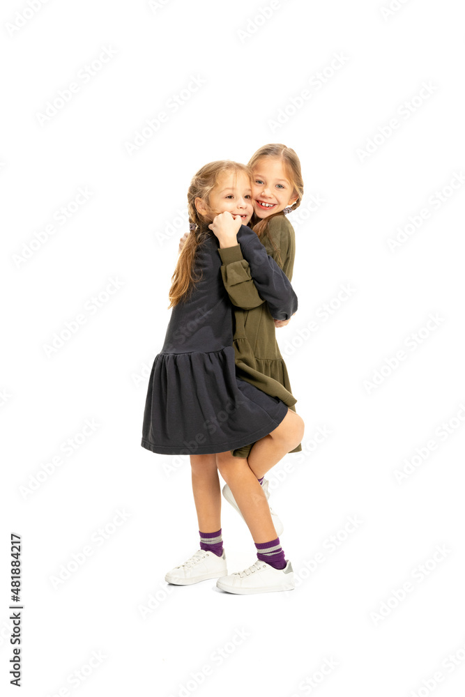 Cheerful little girls, sisters or siblings wearing casual style clothes having fun, playing isolated on white studio background. Concept of childhood, emotions, study