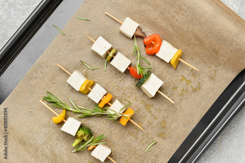 Baking tray with grilled tofu cheese skewers on light background