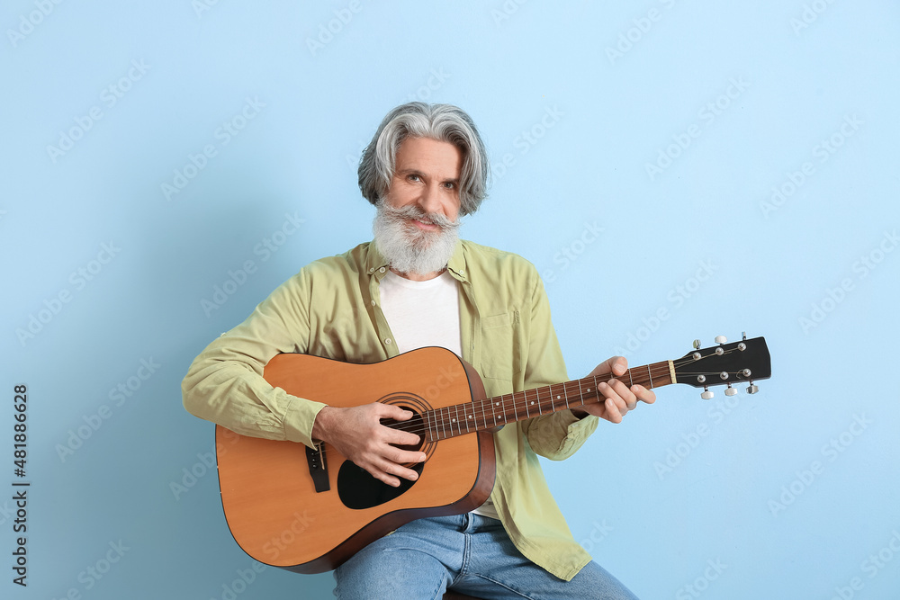 Bearded senior man playing guitar on blue background Bearded senior man playing guitar on blue background