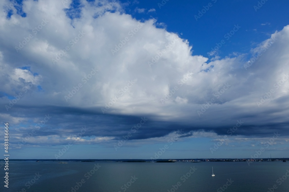 The sky with rolling clouds and  calm surface of sea before storm. Small silhouette of lonely sailing sailboat on sea. Karlskrona coast, Sweden