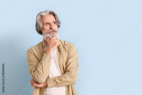 Thoughtful senior man in shirt on blue background © Pixel-Shot
