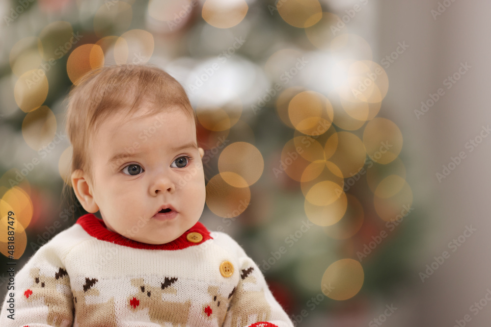 Cute little baby in Christmas sweater against blurred festive lights, space for text. Winter holiday Cute little baby in Christmas sweater against blurred festive lights, space for text. Winter holiday