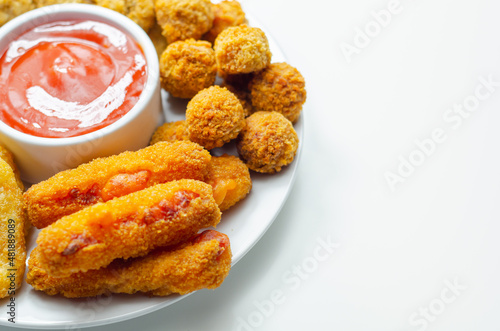 Southern fried and roast chicken bites, onion rings and mozzarella stick served on the white plate with tomato sauce