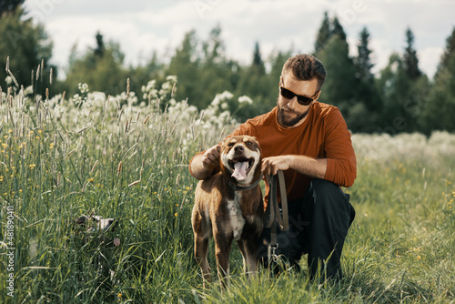 Caucasian man holding red alaskan husky by pet collar in field. Pet owner, adult dog and senior dog in rural.