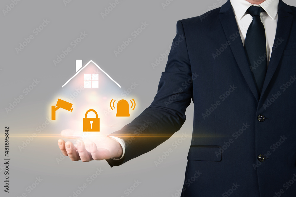 Insurance agent holding a house in the palm of his hand next to several security devices. Home insurance and burglary protection