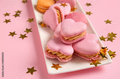 Plate with tasty heart-shaped macaroons and confetti on pink background, closeup