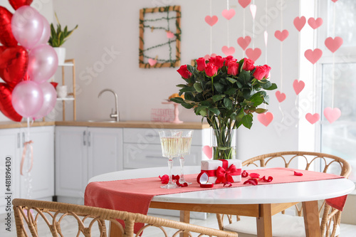 Glasses of champagne  engagement ring  flowers and gift box on dining table in kitchen
