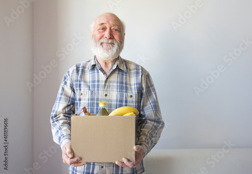 Donation. A pensioner is holding a cardboard box with food from volunteers. Getting social assistance for the elderly during a pandemic.