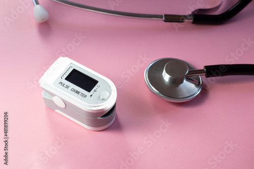 Pulse oximeter and stethoscope on pink background. Medical devices to measure oxygen and blood pressure. 