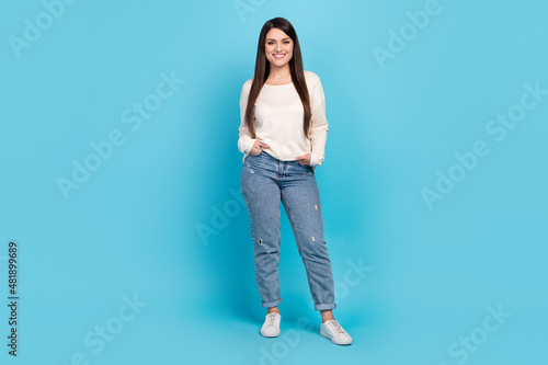 Full size photo of young cheerful girl hands in pocket wear modern outfit isolated over blue color background