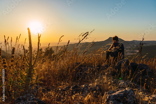 Landscape of a beautiful sunset with a young boy sitting on rocks on the side with a mountain in the background © Manuel