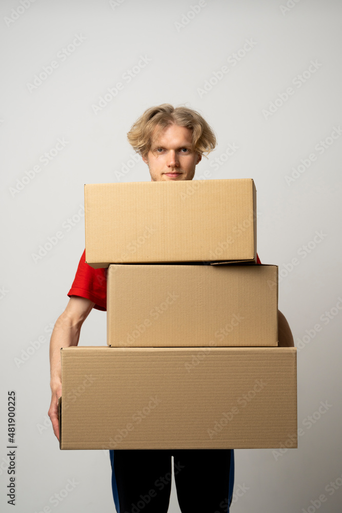 Cheerful delivery man. Happy young courier holding a cardboard boxes and smiling while standing against white background. Delivery man holding pile of cardboard boxes in front of himself. Cheerful delivery man. Happy young courier holding a cardboard boxes and smiling while standing against white background. Delivery man holding pile of cardboard boxes in front of himself.