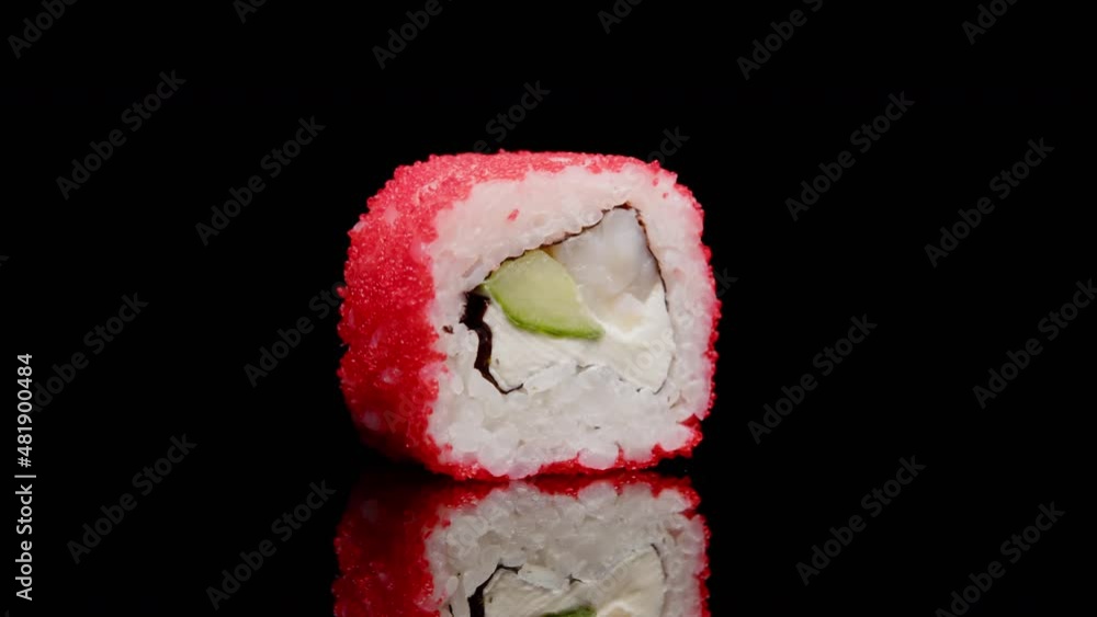 Sushi roll rotates on black background on mirror table with reflection close-up. Fresh roll with shrimp, cream cheese, cucumber, rice topped with red tobiko caviar. Sushi menu, Japanese food. Sushi roll rotates on black background on mirror table with reflection close-up. Fresh roll with shrimp, cream cheese, cucumber, rice topped with red tobiko caviar. Sushi menu, Japanese food.