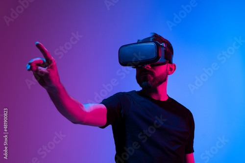 Bearded young man in virtual reality glasses in the studio with blue and pink light. photo