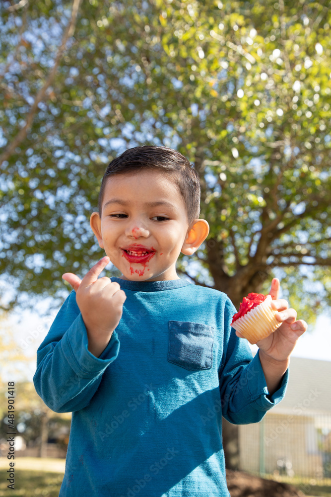 Young boy eating a cupcake with frosting at the park. Young boy eating a cupcake with frosting at the park.