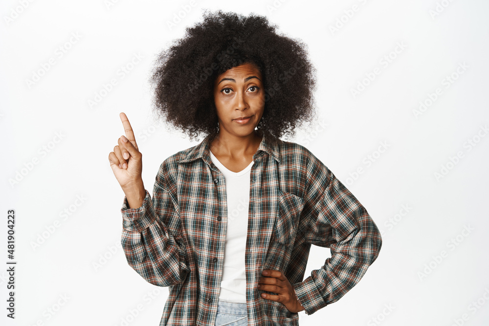 Image of sassy, skeptical african american woman with afro hair, shaking finger, pointing up and staring at camera, standing over white background Image of sassy, skeptical african american woman with afro hair, shaking finger, pointing up and staring at camera, standing over white background