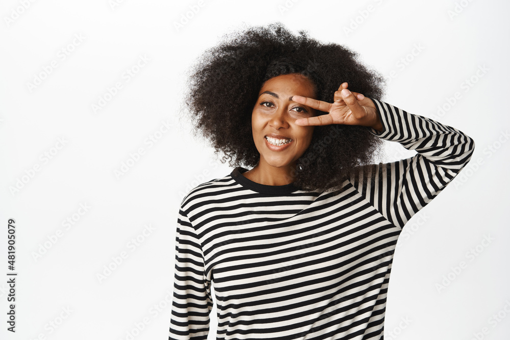 Positive african american female model, showing peace, v-sign gesture and smiling, optimistic and happy face expression, standing over white background Positive african american female model, showing peace, v-sign gesture and smiling, optimistic and happy face expression, standing over white background