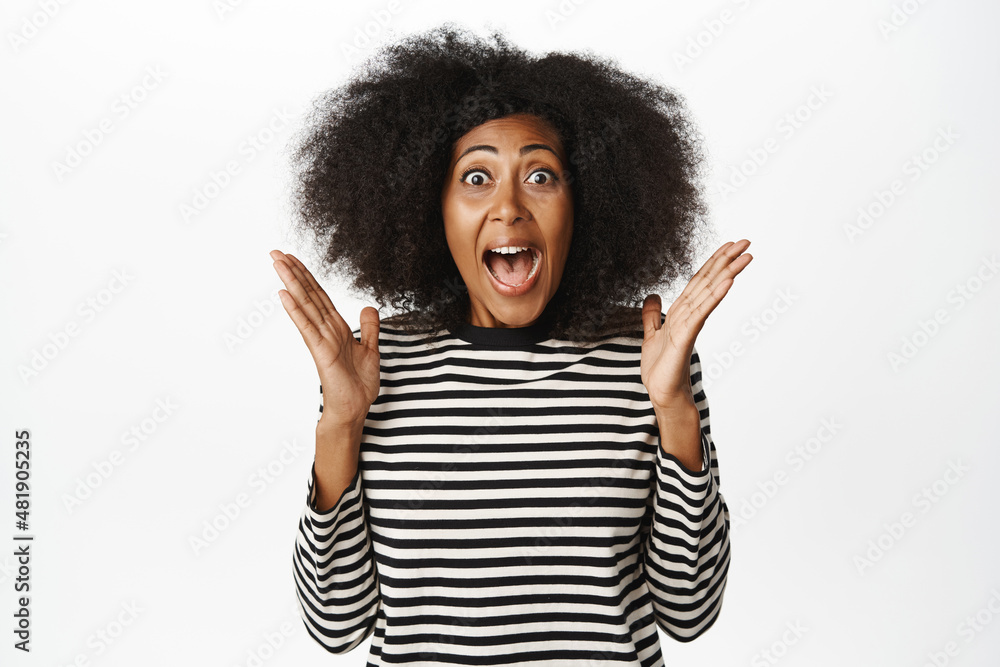 Enthusiastic african american woman celebrating, scream yes, looking amazed and surprised, winning, triumphing over success, standing against white background Enthusiastic african american woman celebrating, scream yes, looking amazed and surprised, winning, triumphing over success, standing against white background