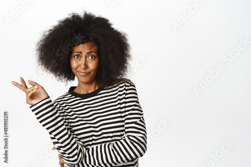 Skeptical african american sassy woman, shaking hand in disapproval, looking with disbelief and doubt, smirking and staring at camera, white background © Cookie Studio
