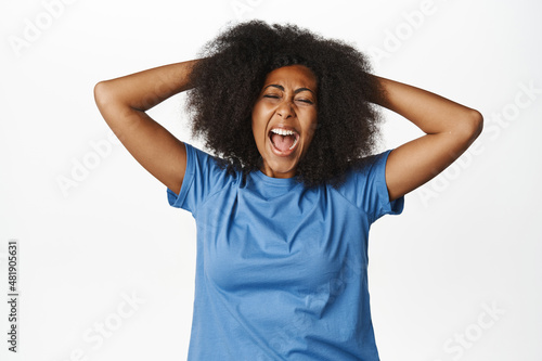 Portrait of distressed african american woman screaming and pulling hair out of head  shouting depressed and upset  feeling sad  standing over white background