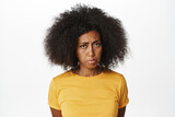 Close up portrait of african american woman sulking, pouting, making upset angry face expression, standing in yellow t-shirt over white background