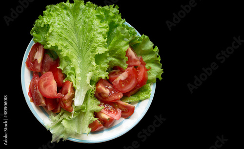 dish with tomatoes and lettuce with water drops frillis isolated on a black background