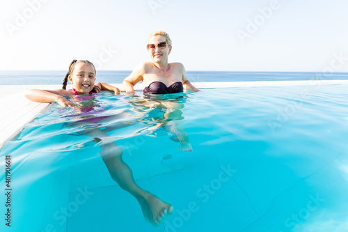 Smiling beautiful woman smears with cream for sunburn little girl near pool in aquapark