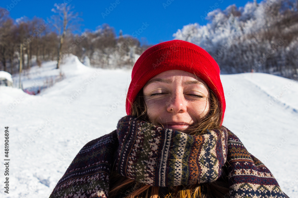 portrait of a person in winter. Woman with red hat smiling in warm clothes and having fun with the snow. Woman enjoying the snow in the mountain. Portrait of a woman in winter