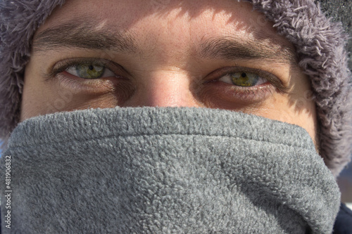 portrait of a person. Close up of green eyed man in warm clothes with hoodie and scarf in winter season. Man looking at camera in close distance.
