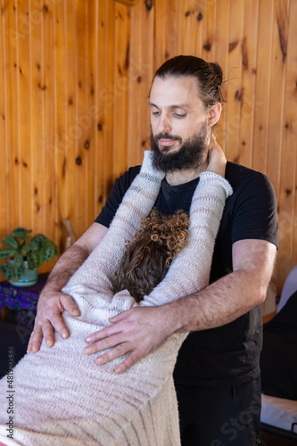 A male physician is seen performing chiropractic technique on woman with back injury. Stretching the erector spinae muscle group. Copy space to left. photo