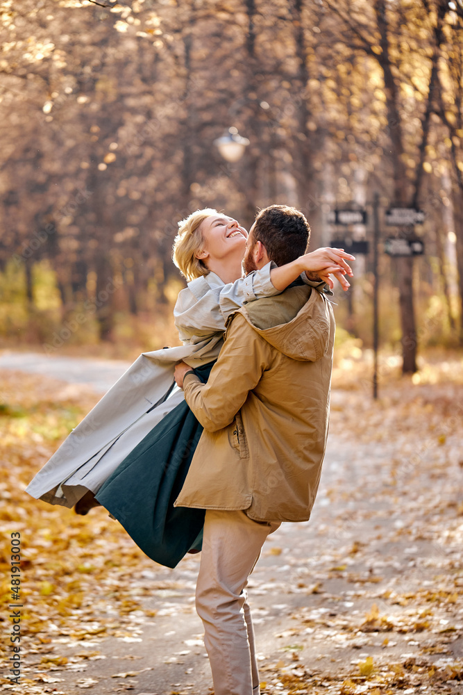 Fototapeta premium Couple walking and hugging in autumn forest, enjoy spending time together, cute caucasian man and woman in coats in love, outdoors, warm weather during leaf fall. carefree and happy. relationships
