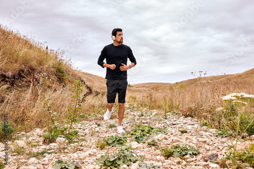 Sportive and fit caucasian sportsman is running forward across the stones in mountains at summer morning, alone. Active workout on fresh air before marathon. Recreation, healthy lifestyle, sport