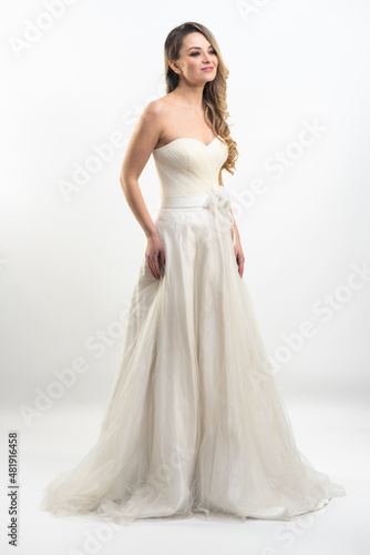 Beautiful attractive bride in wedding dress with long full skirt, white background © alipko