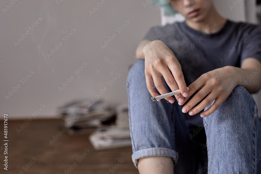 Cropped close-up woman hands holding cigarette in hands while sitting on floor alone at home. unrecognizable sad female is depressed, feeling anxiety, worried about something, smoking. loneliness