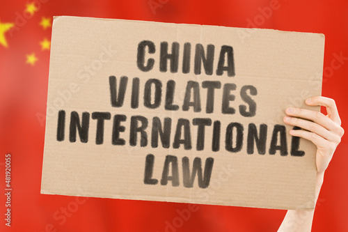 The phrase " China violates international law " on a banner in men's hand with blurred Chinese flag on the background. Political negotiations. Relationship. Illegal actions. Legislation. Conflict