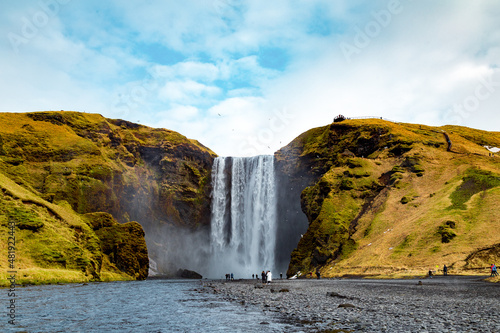 Skogafoss in Iceland with blue skies and green hills