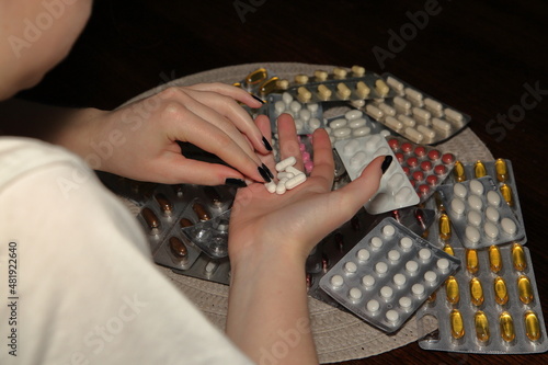 Hands of young girl with pills over blisters with other drugs, tablets and pills on the table