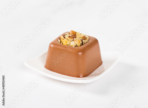 Chocolate nut cream dessert in the shape of a square savarin on a plate on a white background