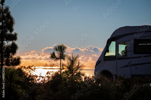 Travel people lifestyle and nomadic life with white camper van motorhome and beautiful colorful sunset on the ocean in background. Travel and enjoy freedom and nature with rv photo