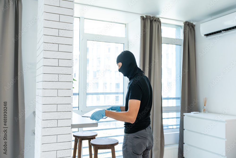 Thief with black balaclava stealing laptop. The burglar commits a crime in Luxury apartment