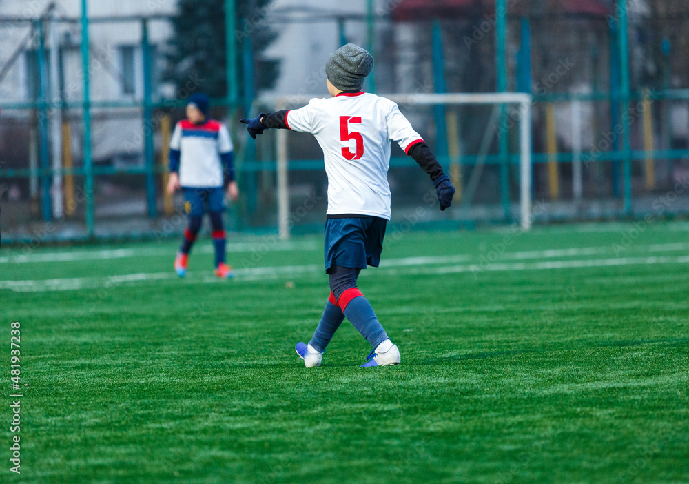 Young sport boys in white sportswear running and kicking a ball on pitch. Soccer youth team plays football. Activities for kids, training Young sport boys in white sportswear running and kicking a ball on pitch. Soccer youth team plays football. Activities for kids, training