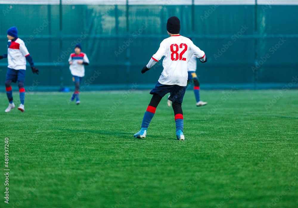 Young sport boys in white sportswear running and kicking a  ball on pitch. Soccer youth team plays football. Activities for kids, training	