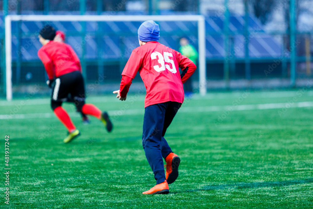 Obraz premium Boy in red white sportswear plays football on field, dribbles ball. Young soccer players teenagers with ball on green grass. 