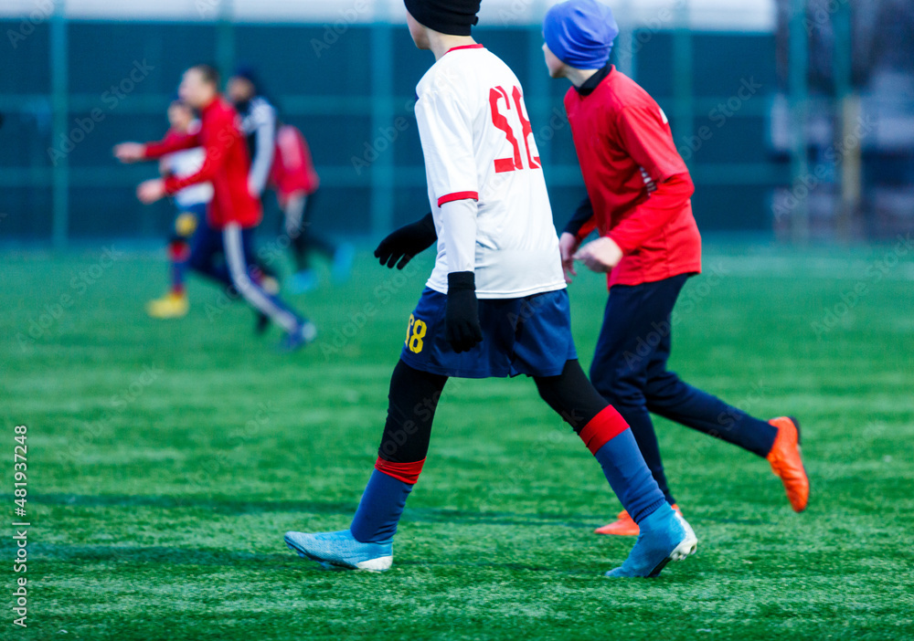 Boy in red white sportswear plays football on field, dribbles ball. Young soccer players teenagers with ball on green grass. 