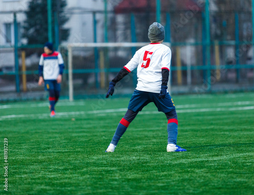 Young sport boys in white sportswear running and kicking a  ball on pitch. Soccer youth team plays football. Activities for kids, training  © Natali