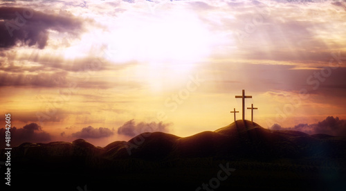 The sky over Golgotha Hill is shrouded in majestic light and clouds, revealing the holy cross symbolizing the death and resurrection of Jesus Christ. 