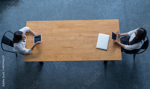 Top view of two Asian work together with sitting in opposite side of table and they use tablet to work with online business.